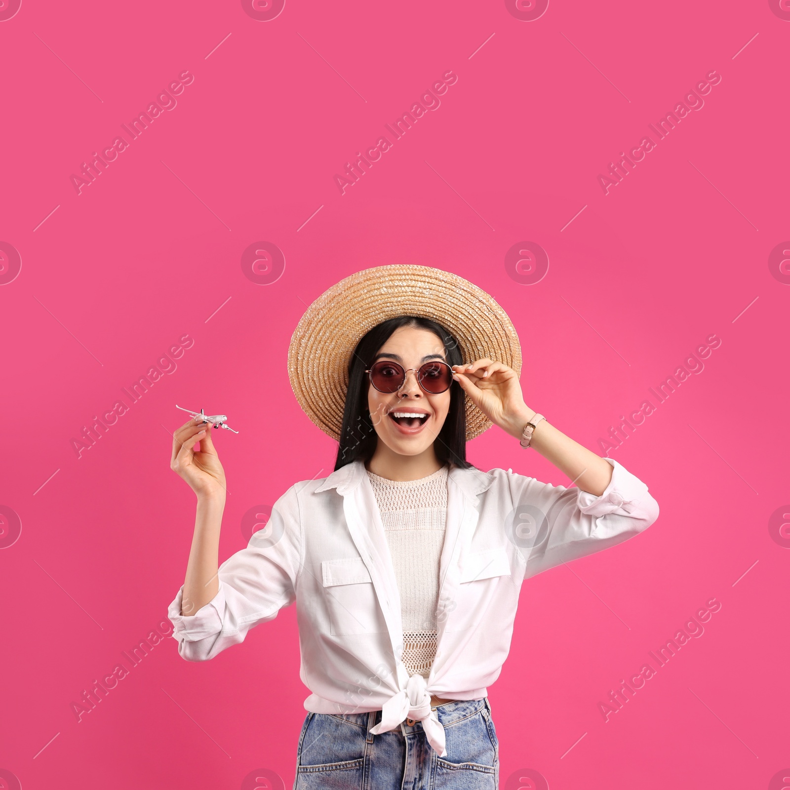 Photo of Happy female tourist with toy plane on pink background