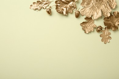 Photo of Golden oak leaves and acorns on beige background, flat lay with space for text. Autumn decor