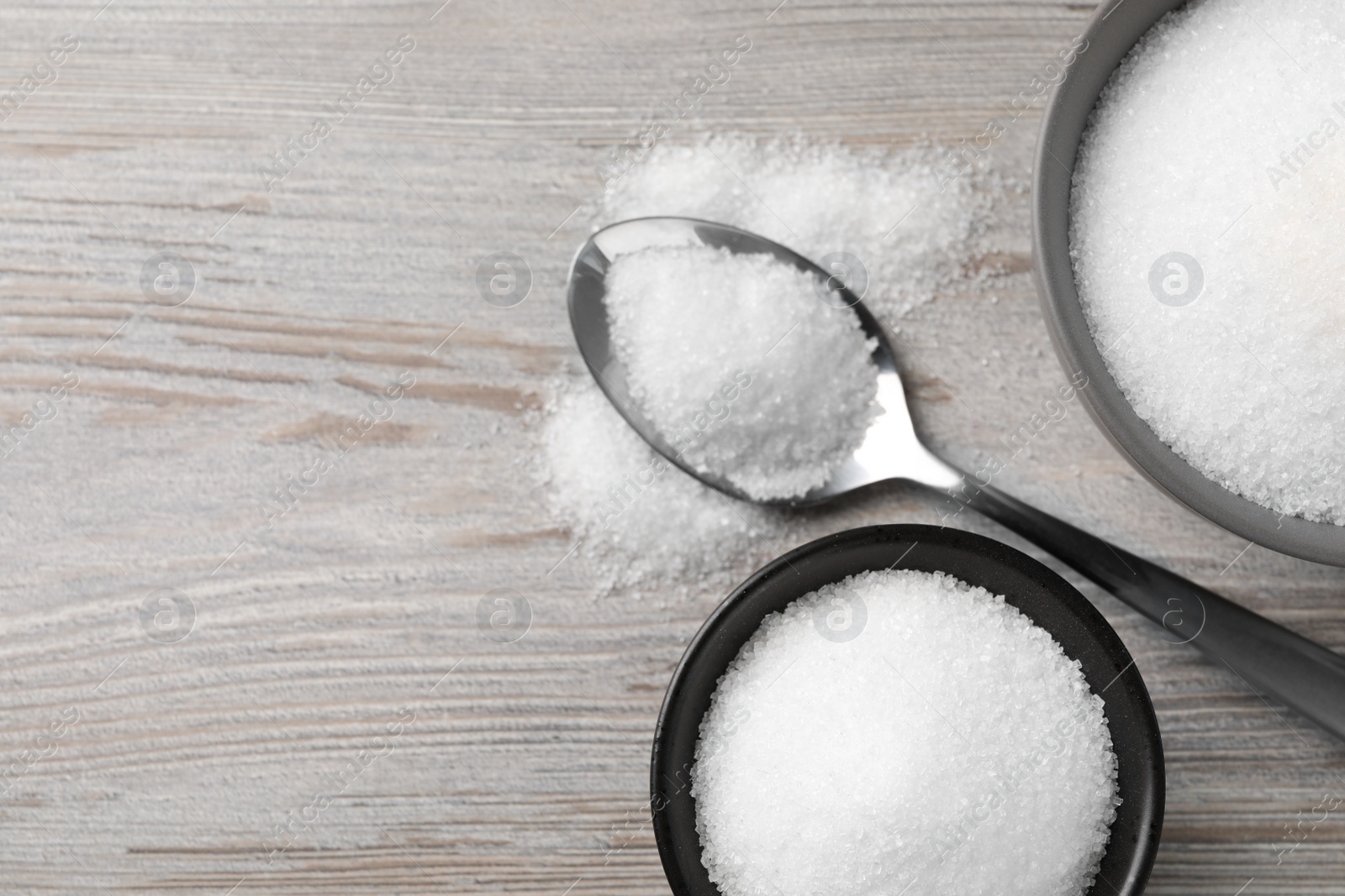 Photo of Granulated sugar on light wooden table, flat lay. Space for text