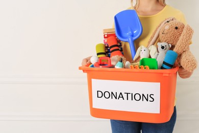 Photo of Woman holding donation box with child toys against light background, closeup. Space for text