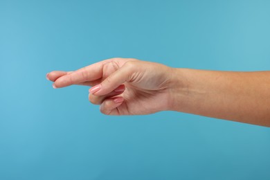 Photo of Woman crossing her fingers on light blue background, closeup