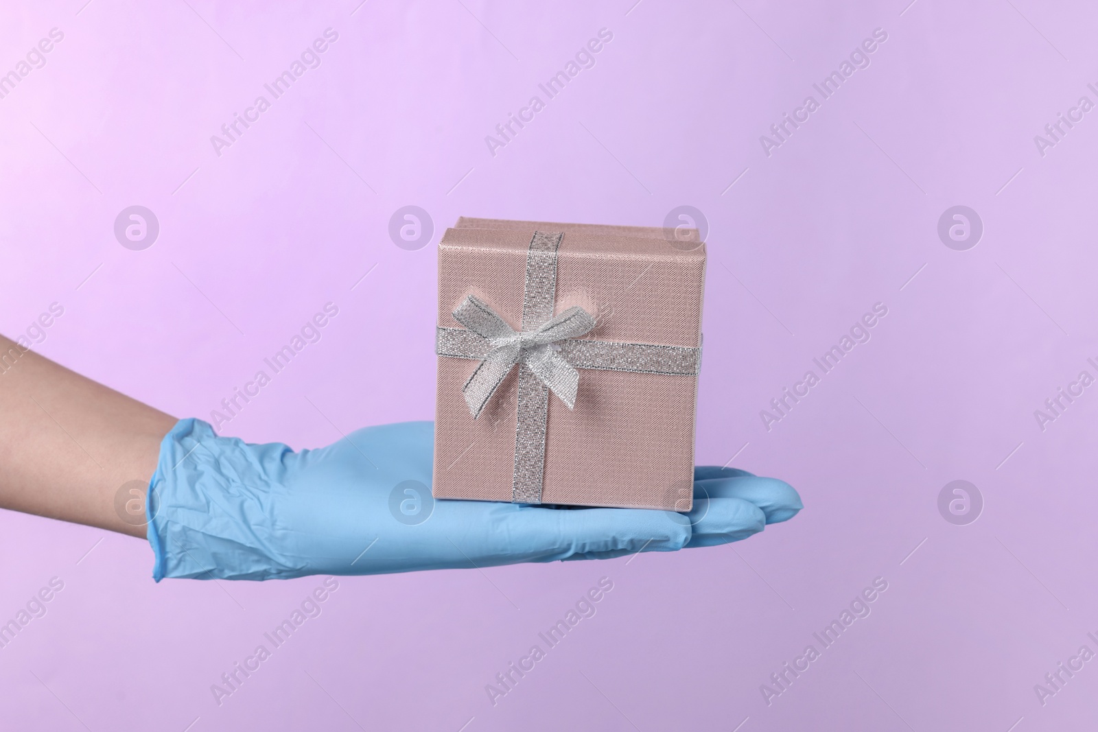 Photo of Doctor holding gift box on violet background, closeup. Medical present