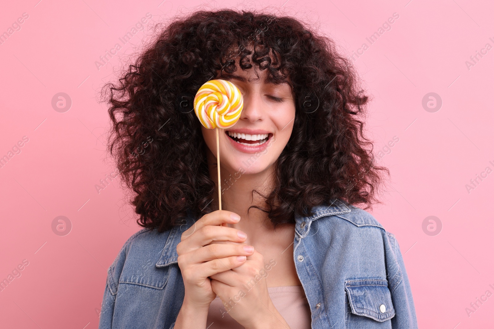 Photo of Beautiful woman covering eye with lollipop on pink background