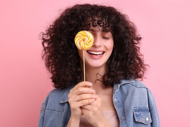 Photo of Beautiful woman covering eye with lollipop on pink background