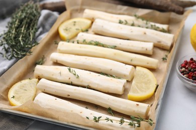 Baking tray with raw salsify roots, lemon and thyme on white marble table, closeup