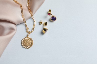 Elegant necklace, earrings and beige cloth on white table, flat lay. Space for text