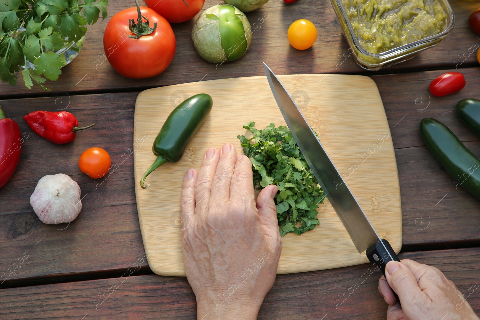 Photo of Woman cutting cilantro for salsa sauce at wooden table, top view