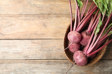 Raw ripe beets in wicker bowl on wooden table, top view. Space for text