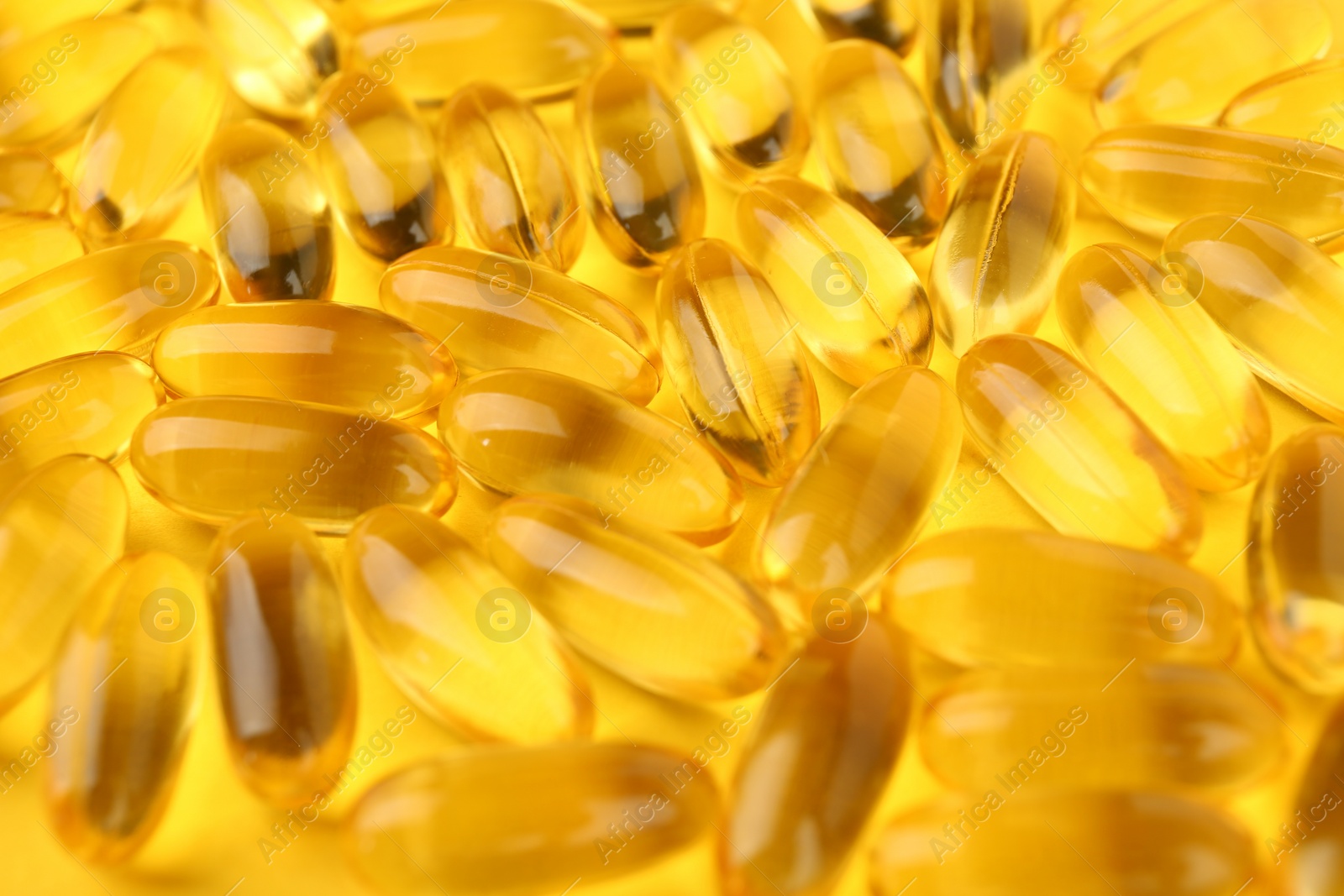 Photo of Many vitamin capsules on yellow background, closeup