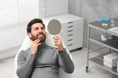 Photo of Man looking at his new dental implants in mirror indoors