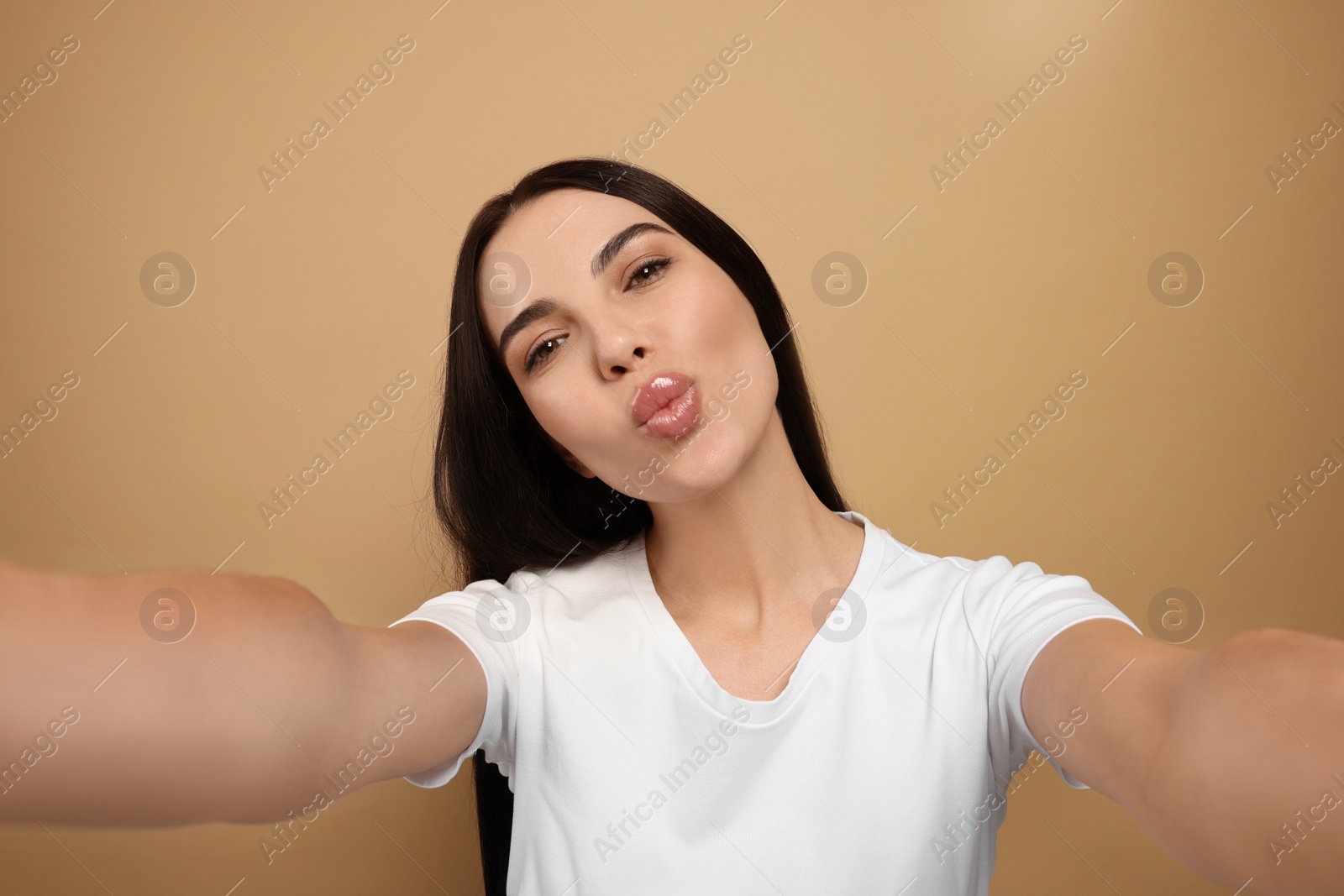 Photo of Beautiful young woman taking selfie while blowing kiss on beige background