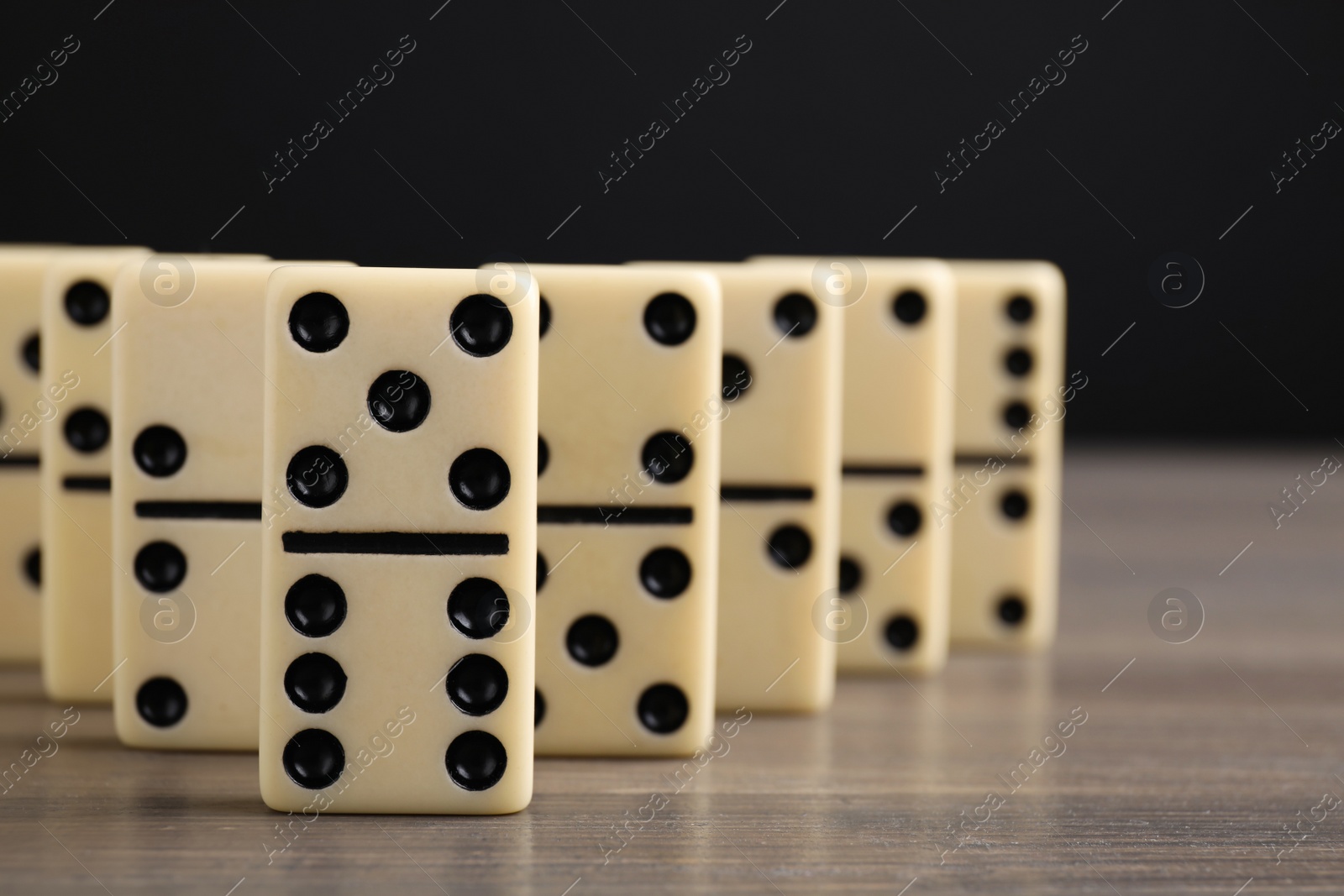 Photo of Domino tiles on wooden table against black background, closeup. Space for text