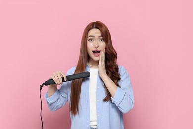 Emotional woman with hair iron on pink background