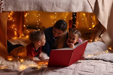 Mother and her children reading book in play tent at home