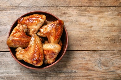 Photo of Bowl with delicious fried chicken wings on wooden table, top view. Space for text