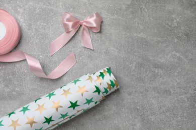 Roll of festive wrapping paper and pink satin ribbon on grey table, flat lay. Space for text