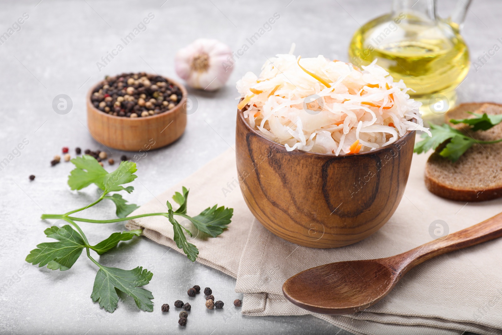 Photo of Bowl of tasty sauerkraut and ingredients on grey table