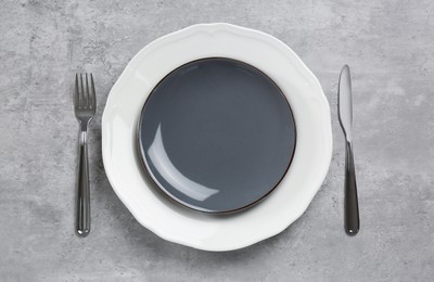 Photo of Ceramic plates, fork and knife on light grey table, flat lay