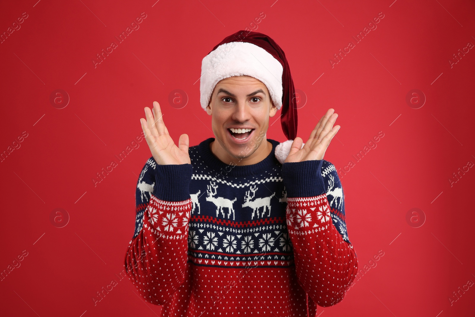 Photo of Excited man in Christmas sweater and Santa hat on red background