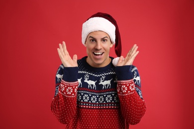 Photo of Excited man in Christmas sweater and Santa hat on red background