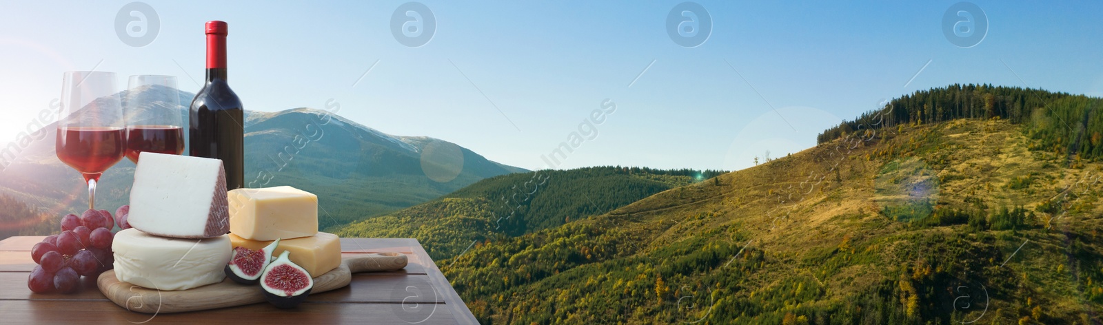 Image of Tasty wine, grapes and cheeses on wooden table against beautiful mountain landscape, space for text. Banner design