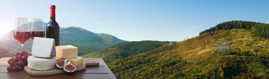 Tasty wine, grapes and cheeses on wooden table against beautiful mountain landscape, space for text. Banner design