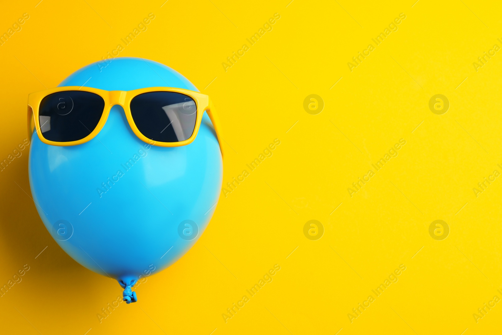 Photo of Balloon with sunglasses on yellow background, top view. Space for text