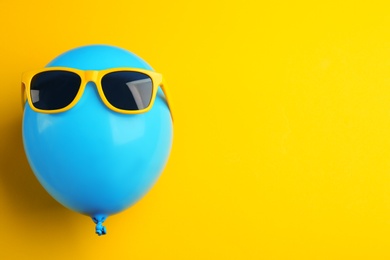 Photo of Balloon with sunglasses on yellow background, top view. Space for text