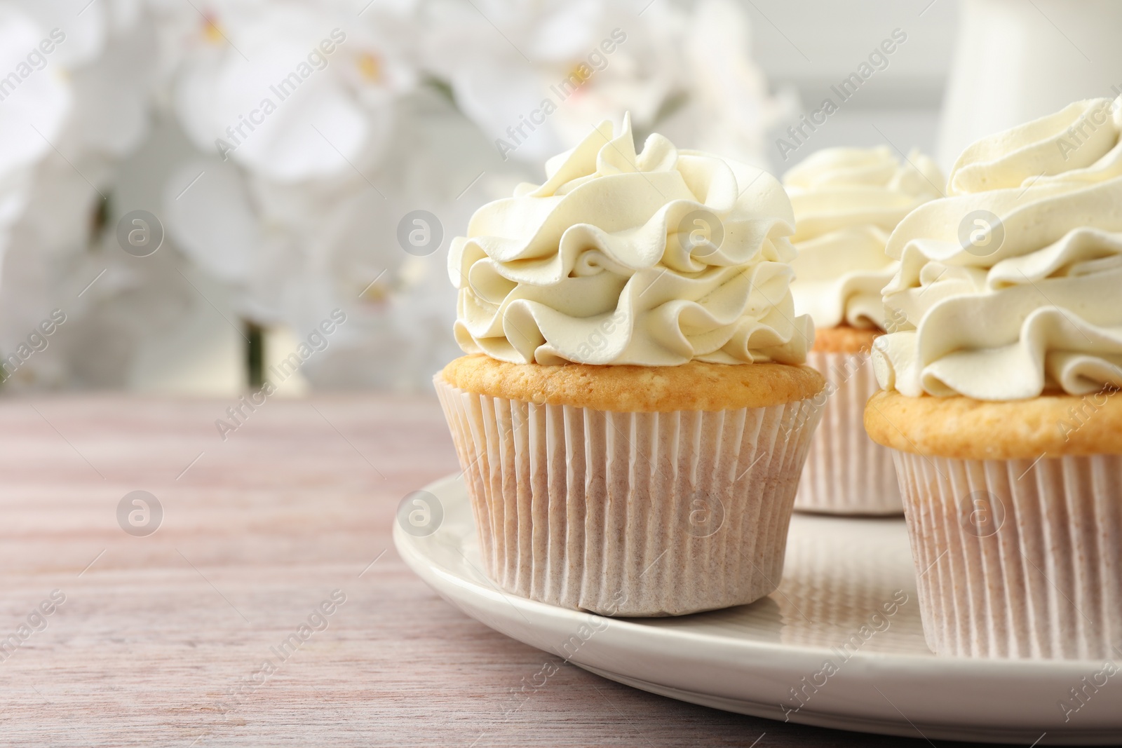 Photo of Tasty cupcakes with vanilla cream on pink wooden table, closeup. Space for text