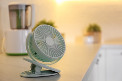 Photo of Modern portable fan on countertop in kitchen, space for text. Summer heat