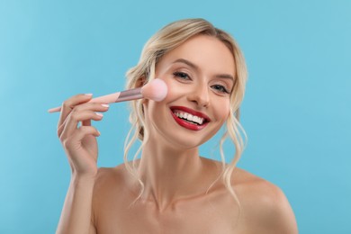 Photo of Beautiful makeup. Smiling woman with brush on light blue background