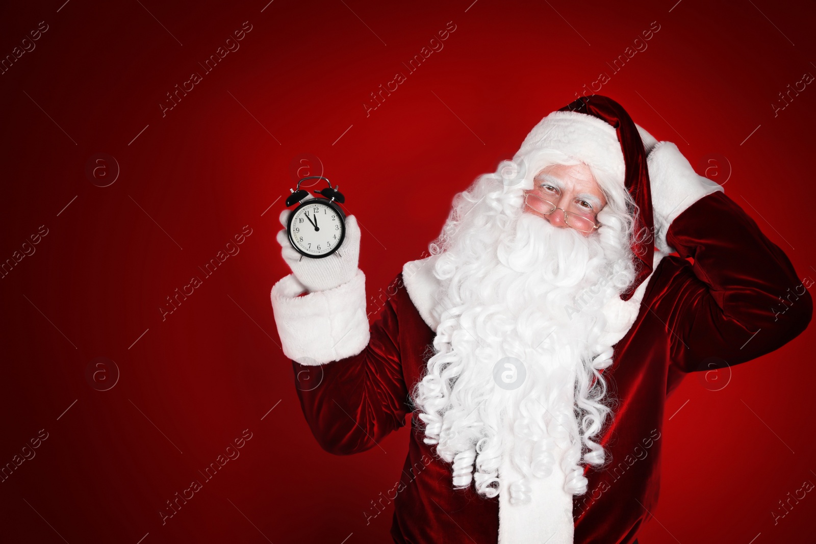 Photo of Santa Claus holding alarm clock on red background. Christmas countdown