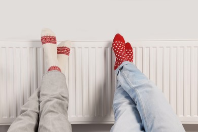 People warming feet near heating radiator indoors, closeup