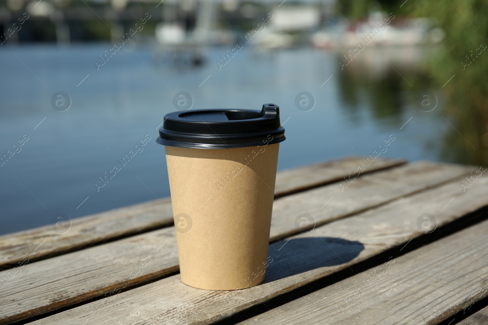 Photo of Takeaway cardboard coffee cup with plastic lid on wooden pier near river