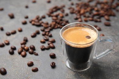 Photo of Cup of tasty espresso and scattered coffee beans on grey table. Space for text
