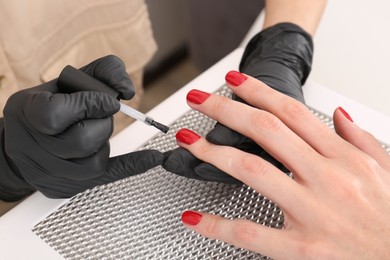 Photo of Professional manicurist working with client at white table, closeup
