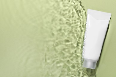 Photo of Tube of facial cleanser in water against olive background, top view. Space for text