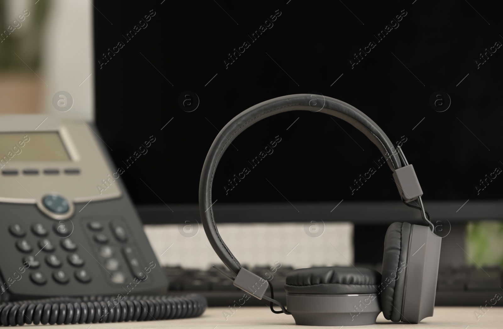 Photo of Modern headphones, desktop telephone and computer on table indoors, space for text