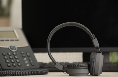 Modern headphones, desktop telephone and computer on table indoors, space for text