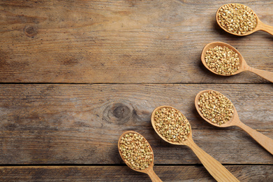 Photo of Uncooked green buckwheat grains in spoons on wooden table, flat lay. Space for text