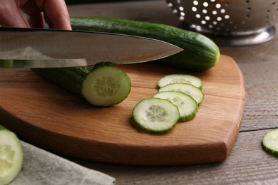 Photo of Woman cutting cucumber on wooden board at table, closeup