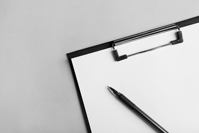 Photo of Black clipboard with sheet of blank paper and pen on light grey background, top view. Space for text