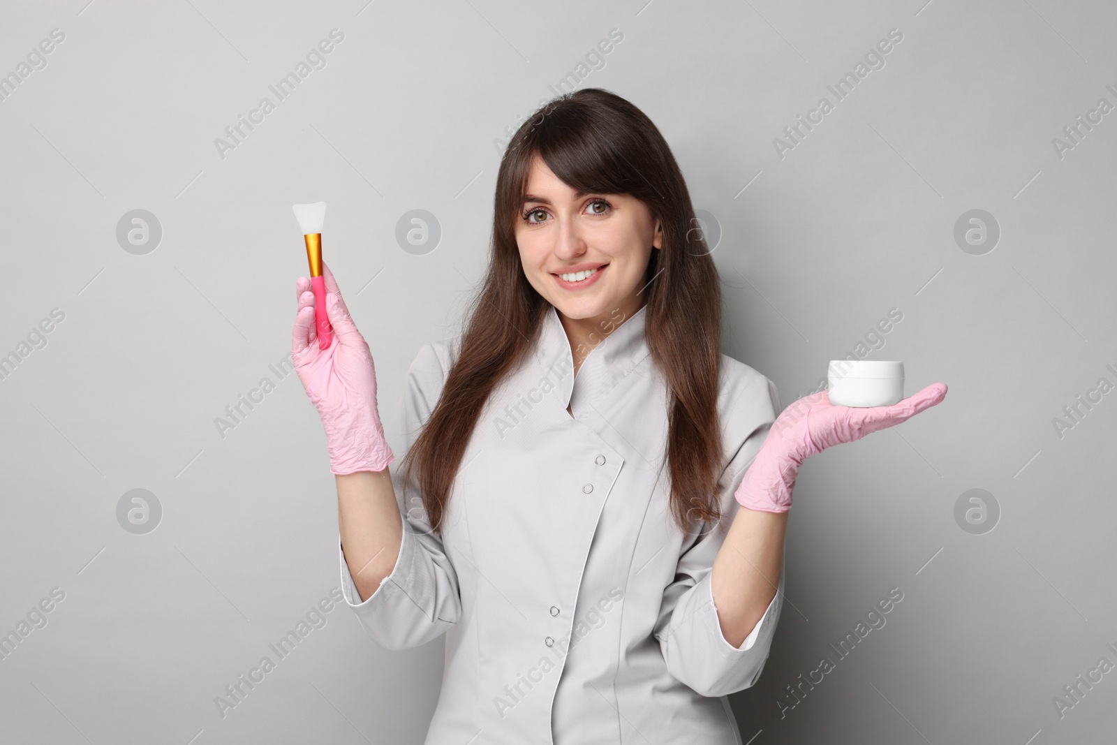 Photo of Cosmetologist with silicone brush and cosmetic product on grey background