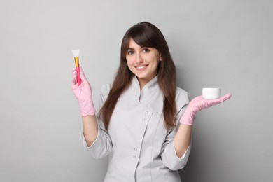 Cosmetologist with silicone brush and cosmetic product on grey background