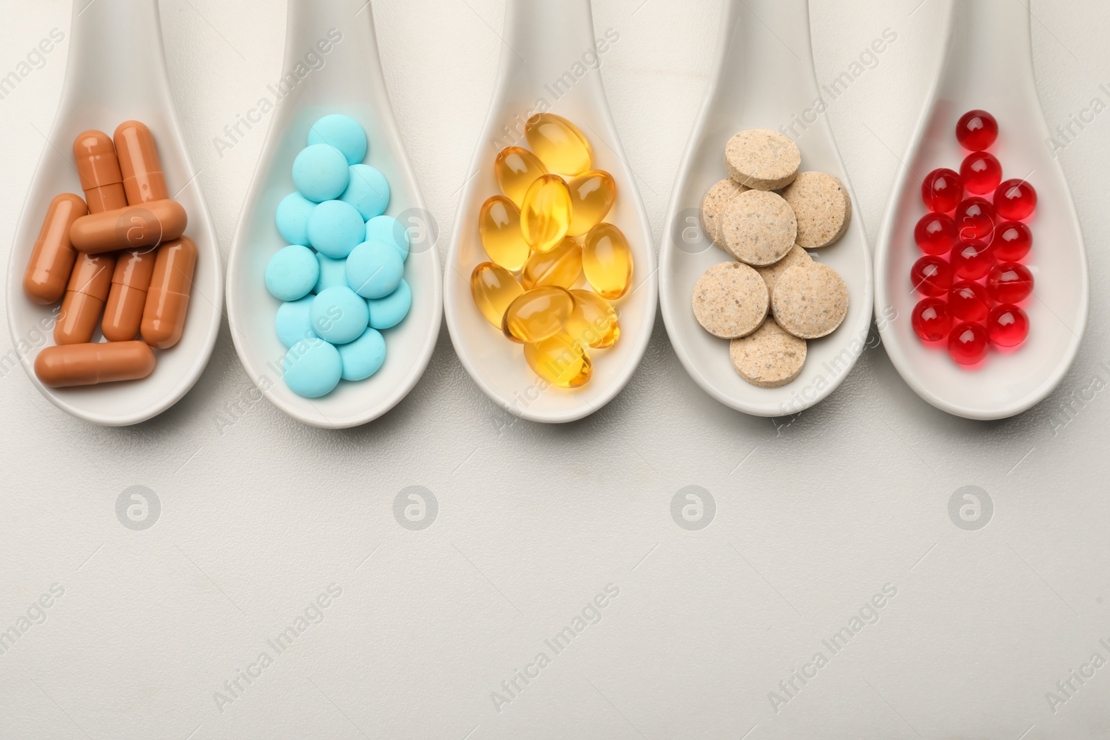 Photo of Spoons with different dietary supplements on white table, flat lay. Space for text