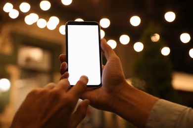 Photo of Man using modern mobile phone outdoors at night, closeup