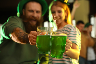 Young woman and man toasting with green beer in pub, focus on glasses. St. Patrick's Day celebration