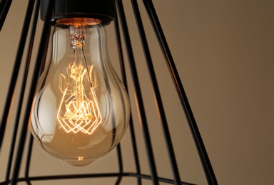 Hanging lamp bulb in chandelier against beige background, closeup