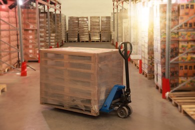 Image of Modern manual forklift with wrapped wooden pallets in warehouse