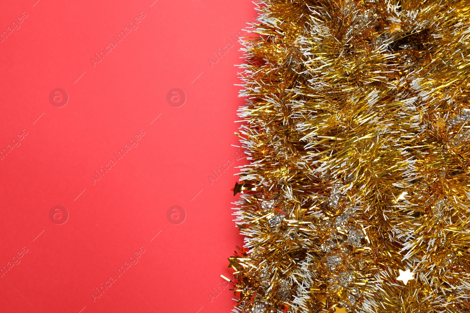 Photo of Shiny golden tinsel on red background, top view. Space for text